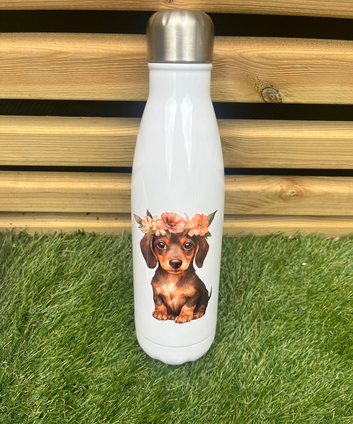 White water bottle with a dachshund design wearing a flower crown on grass and wooden background
