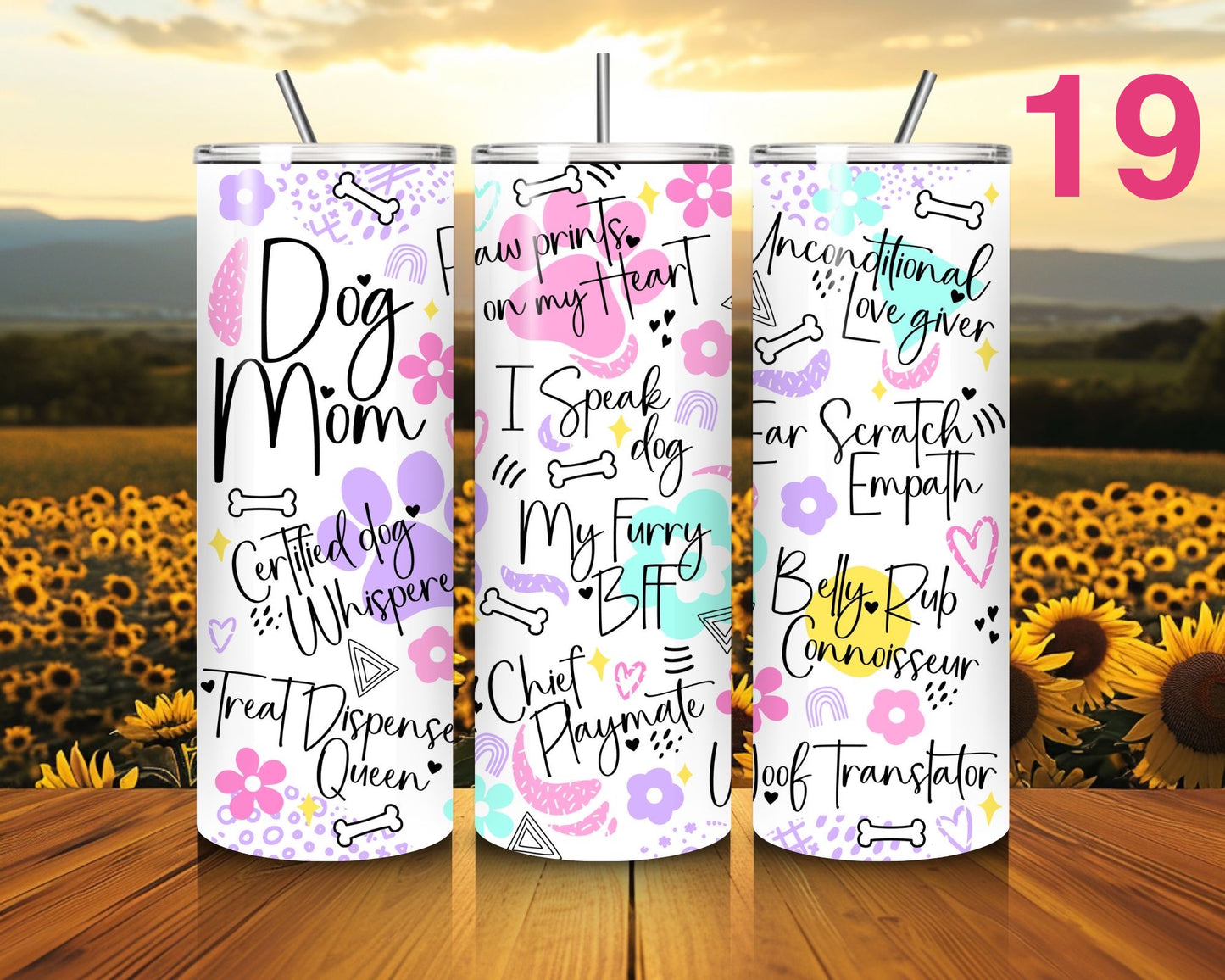 Three tumblers with dog-themed text designs on a wooden surface with a sunflower field background.