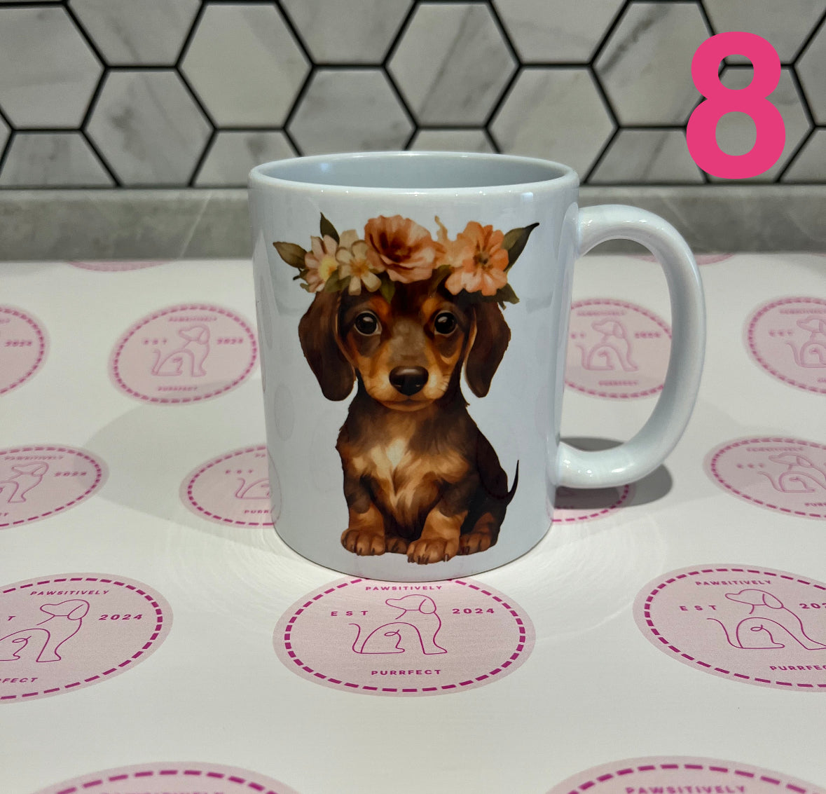 White mug with a dachshund illustration wearing a flower crown on a patterned surface.