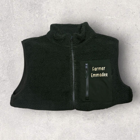 Black fleece gilet with 'Farmer Emmadee' text on a light gray background