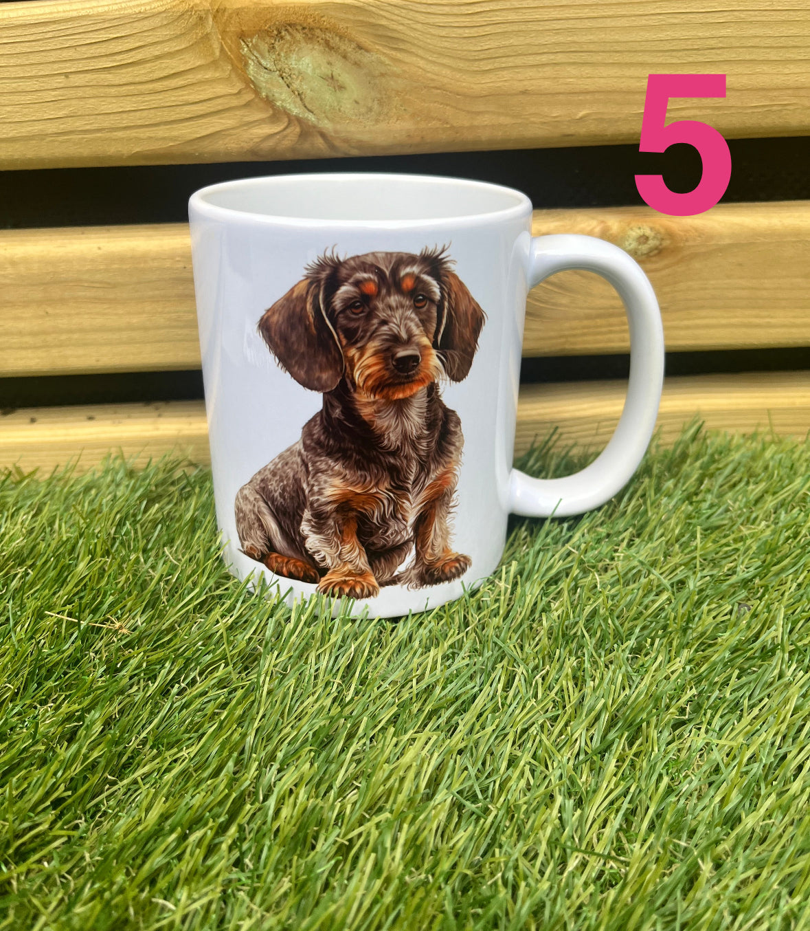 White mug with a dachshund design on grass with a wooden fence in the background
