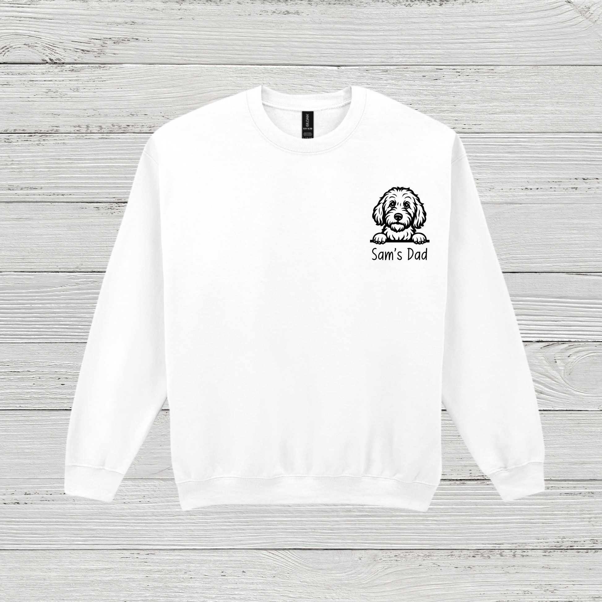 White sweatshirt with a dog illustration and 'Sam's Dad' text on a wooden surface
