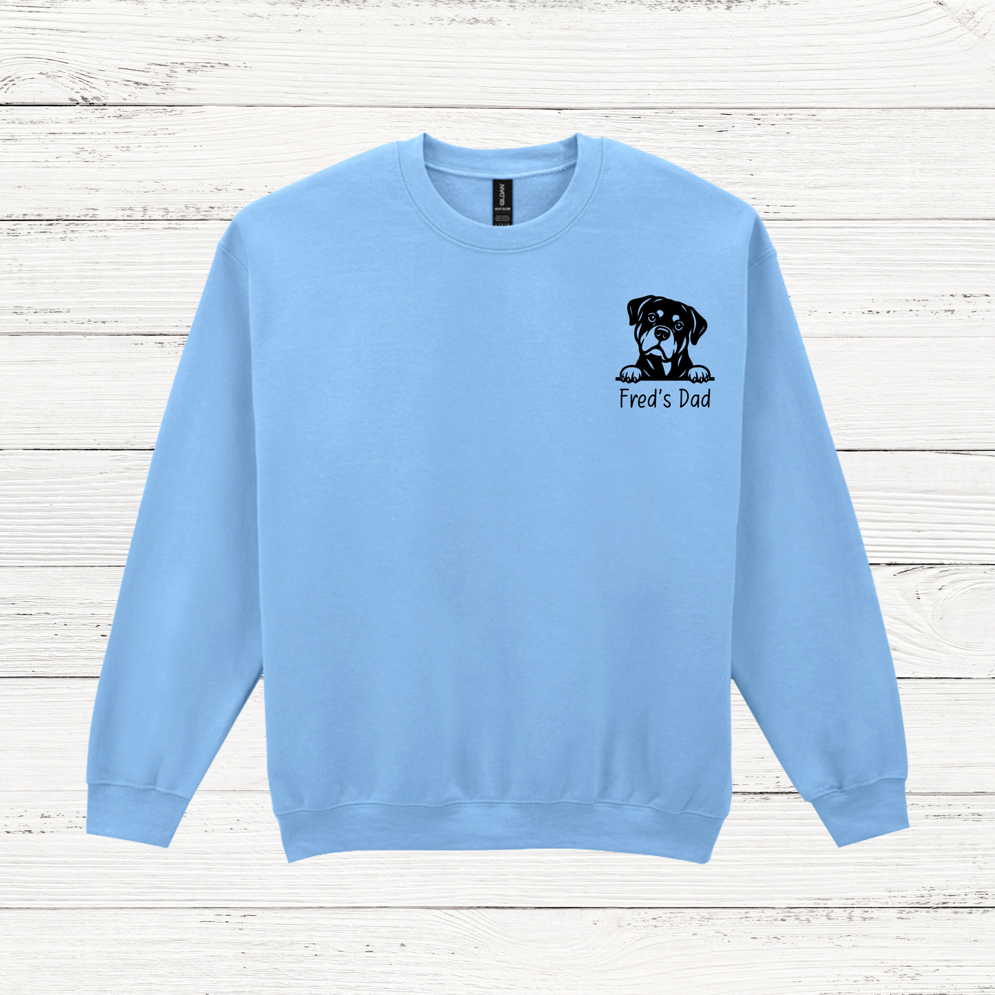 Light blue sweatshirt with a dog graphic and text on a wooden surface