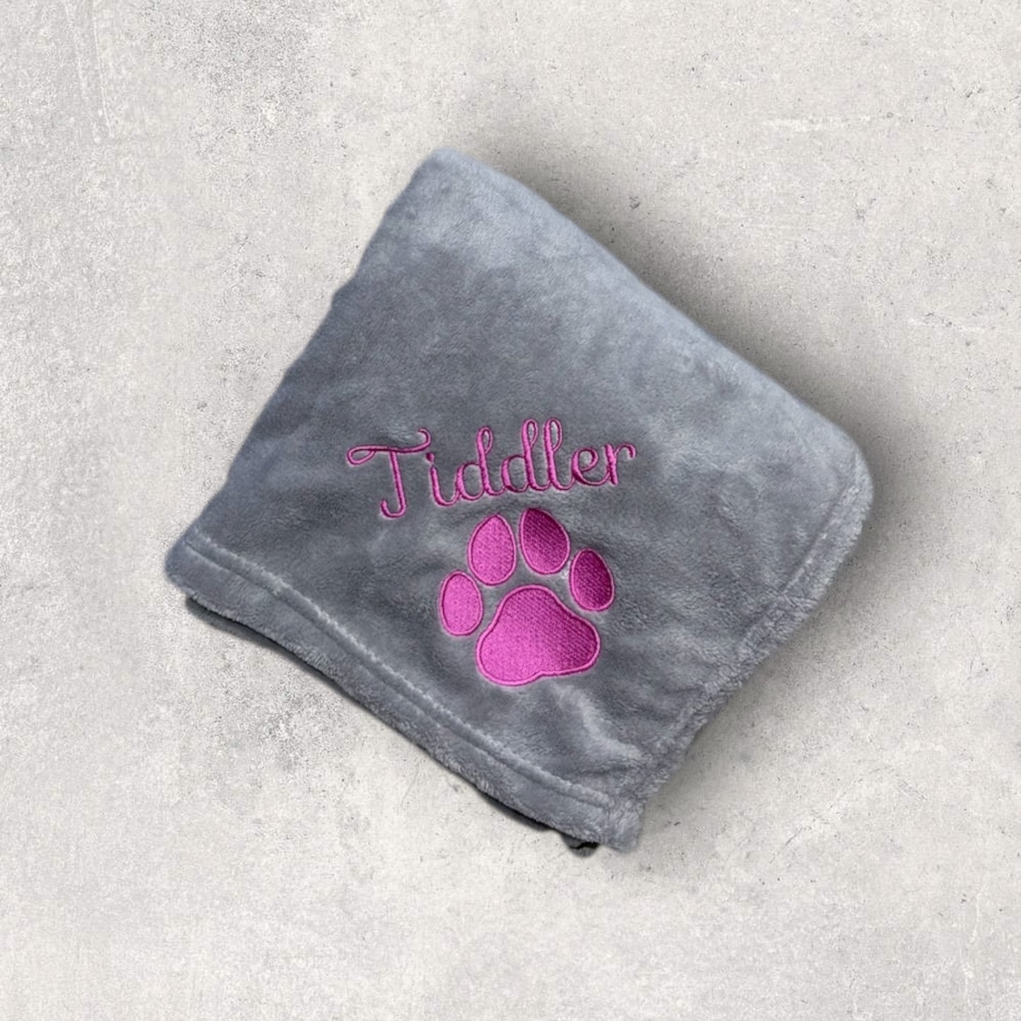 Gray blanket with pink paw print and 'Tiddler' text on a light gray background