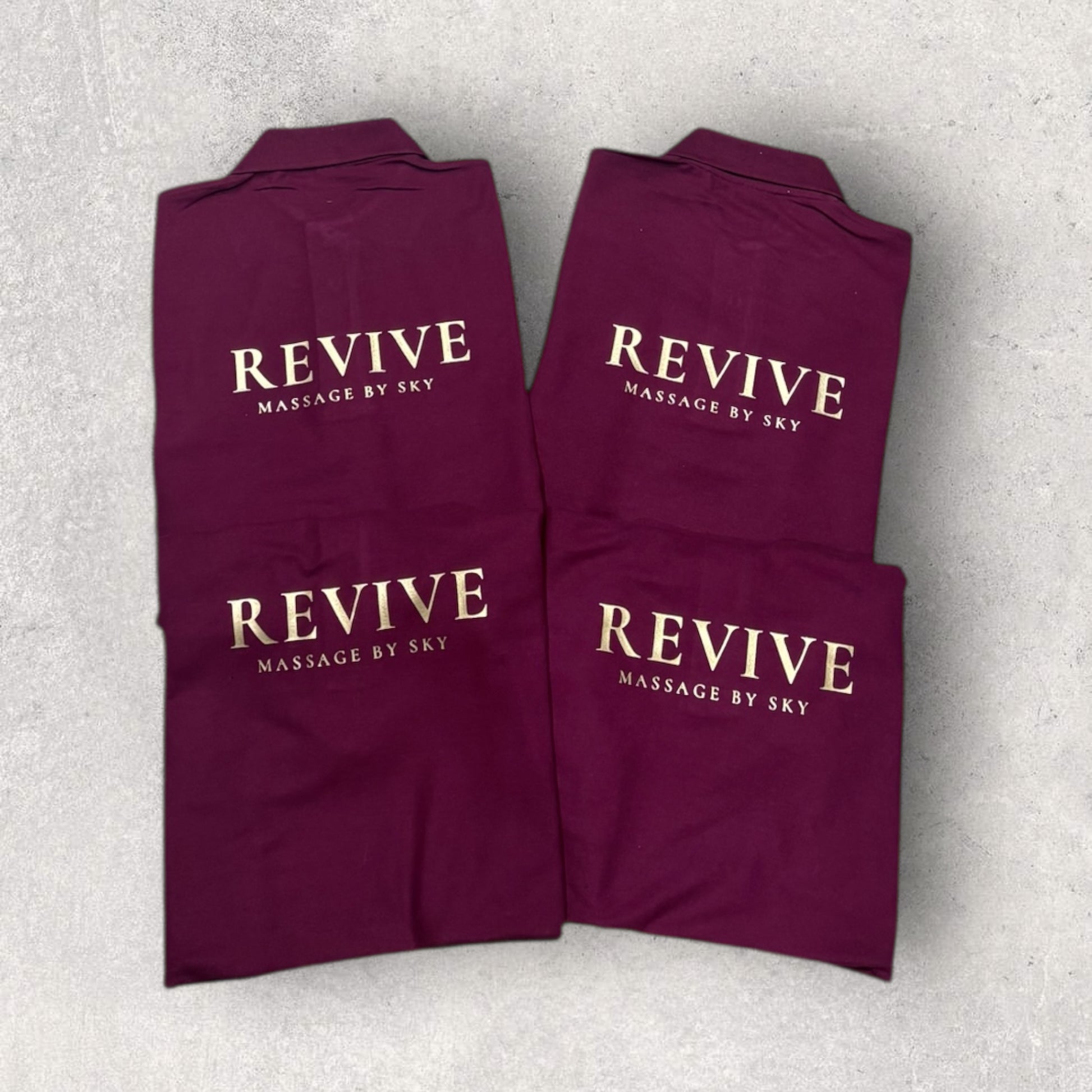 Folded maroon towels with 'REVIVE Massage by Sky' text on a light gray background