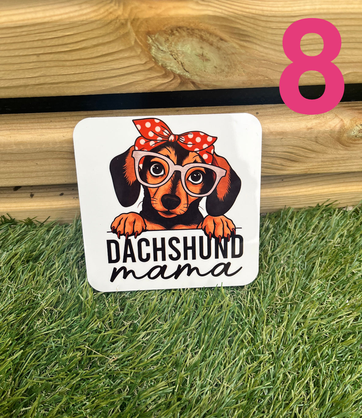 Sticker of a dachshund wearing glasses and a bandana with 'Dachshund Mama' text on grass and wooden surface.
