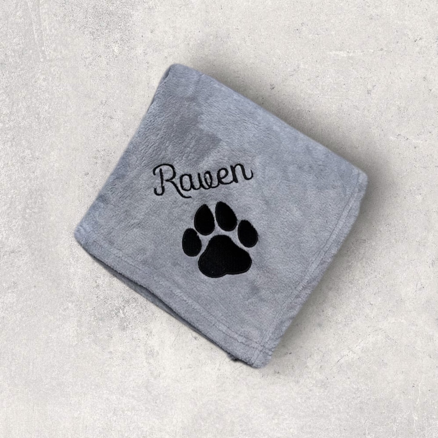 Gray towel with black paw print and 'Raven' text on a light gray background