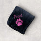 Black blanket with pink paw print and 'Pearl' text on a gray surface