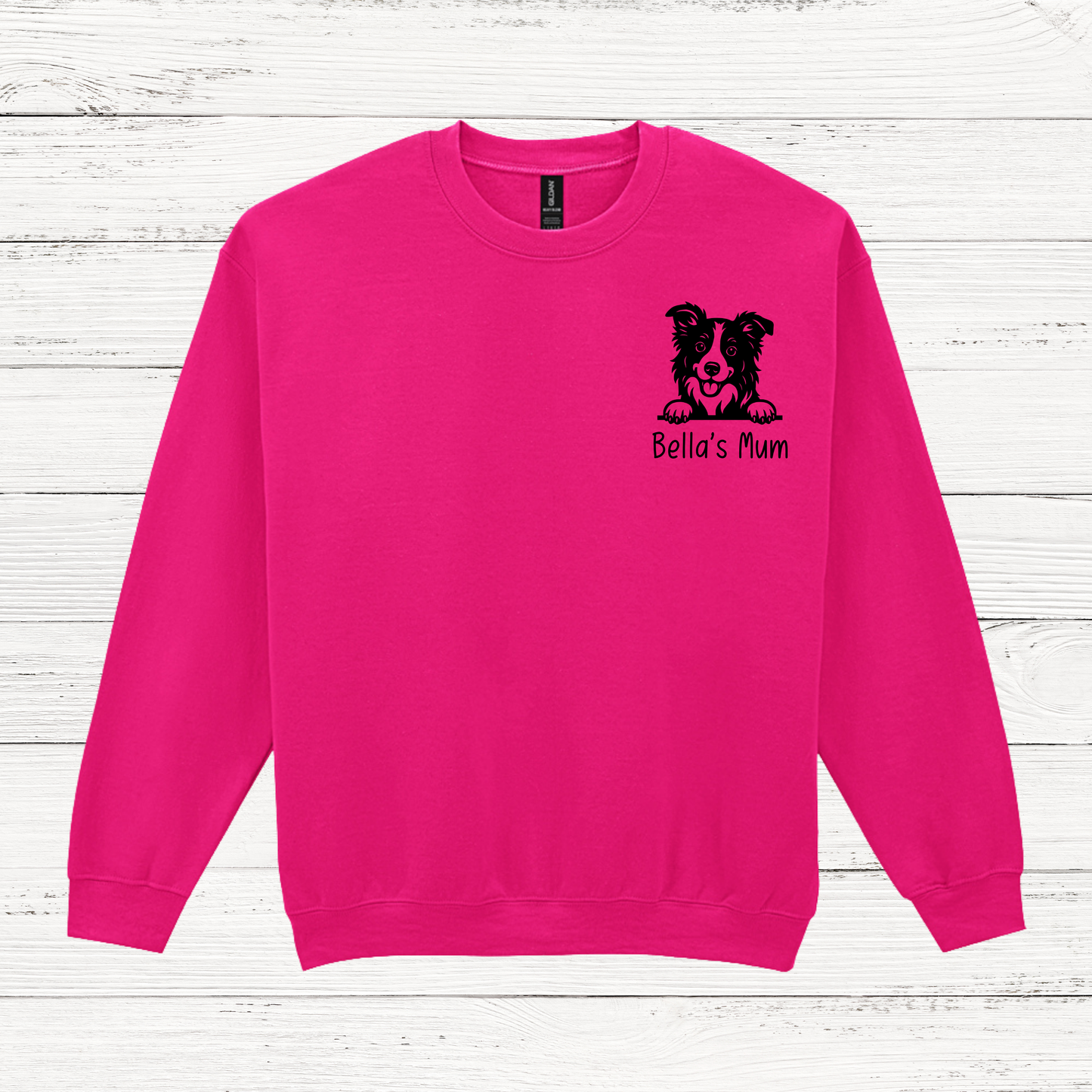 Pink sweatshirt with a black dog illustration and 'Bella's Mum' text on a white wooden background
