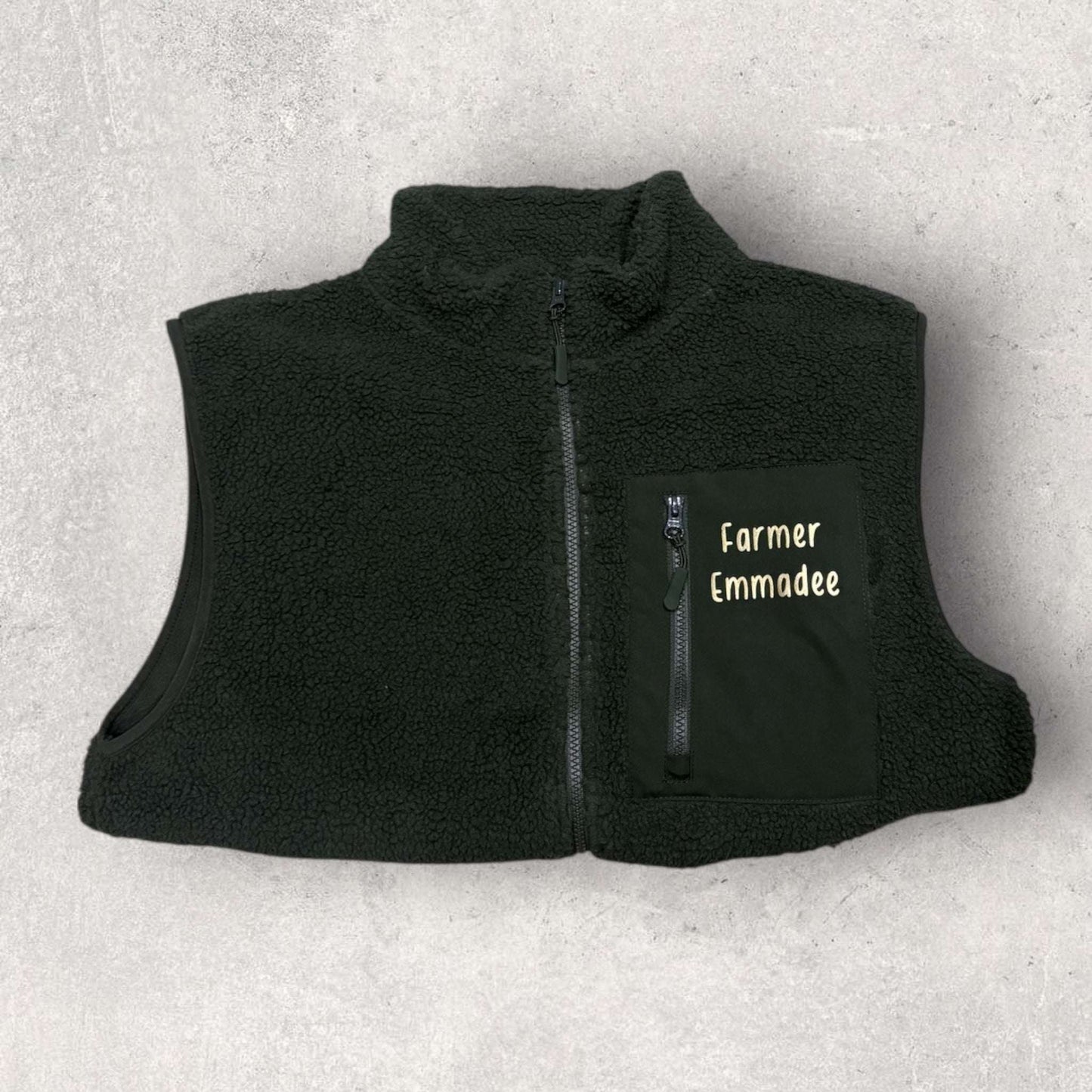 Black fleece gilet with 'Farmer Emmadee' text on a light gray background