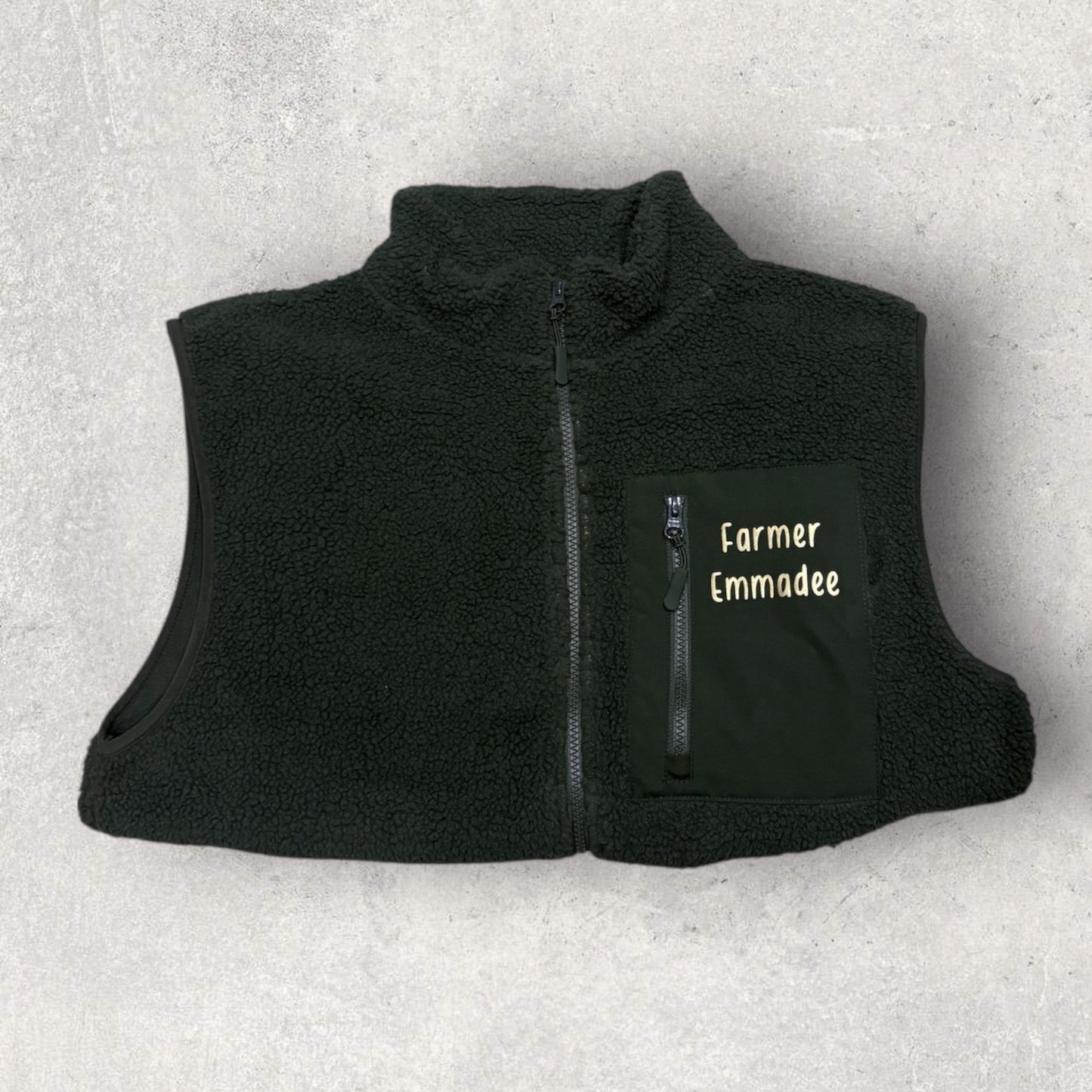 Black fleece gilet with 'Farmer Emmadee' text on a light gray background