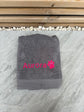 Gray towel with 'Aurora' and a paw print in pink on a stone surface.