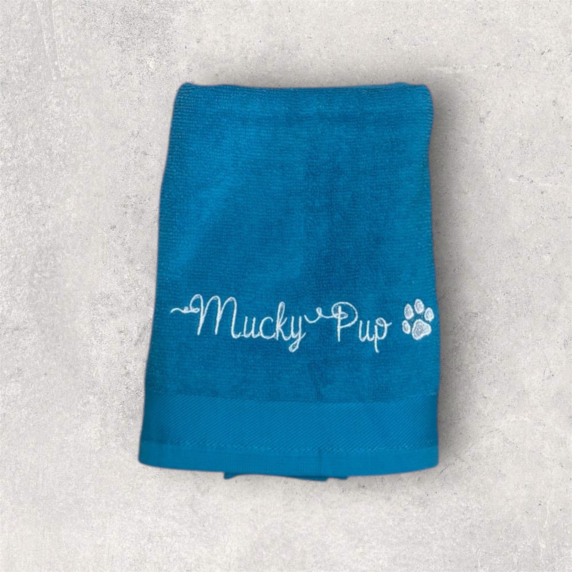 Blue towel with 'Mucky Pup' text on a textured gray background