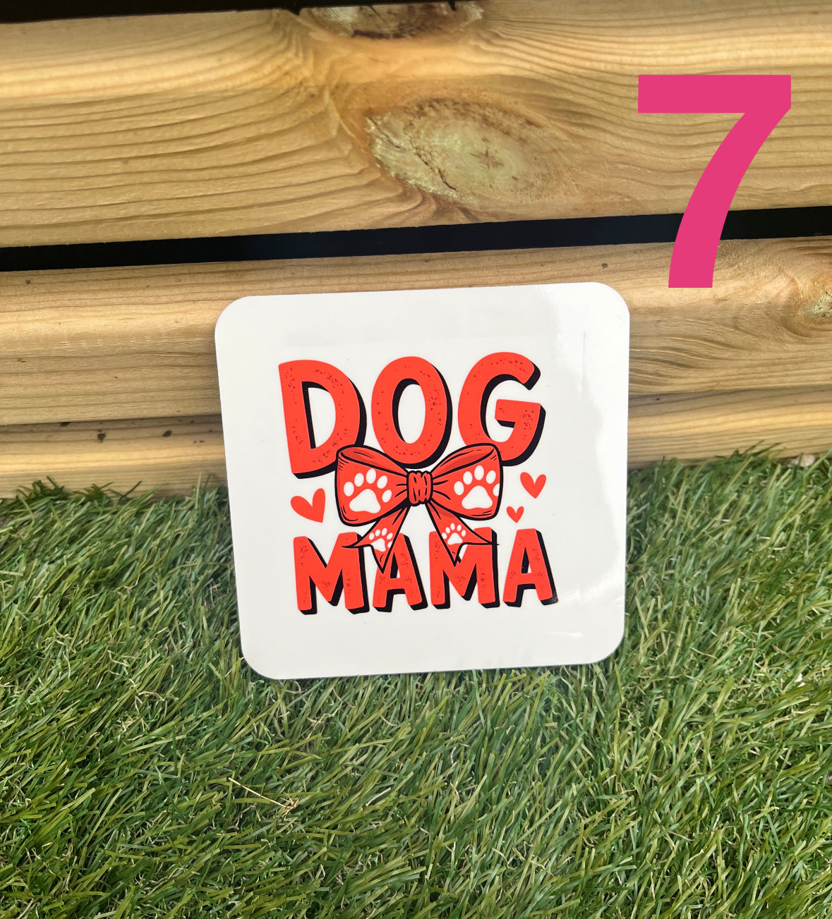 White sign with 'DOG MAMA' text and red graphics on grass and wooden surface