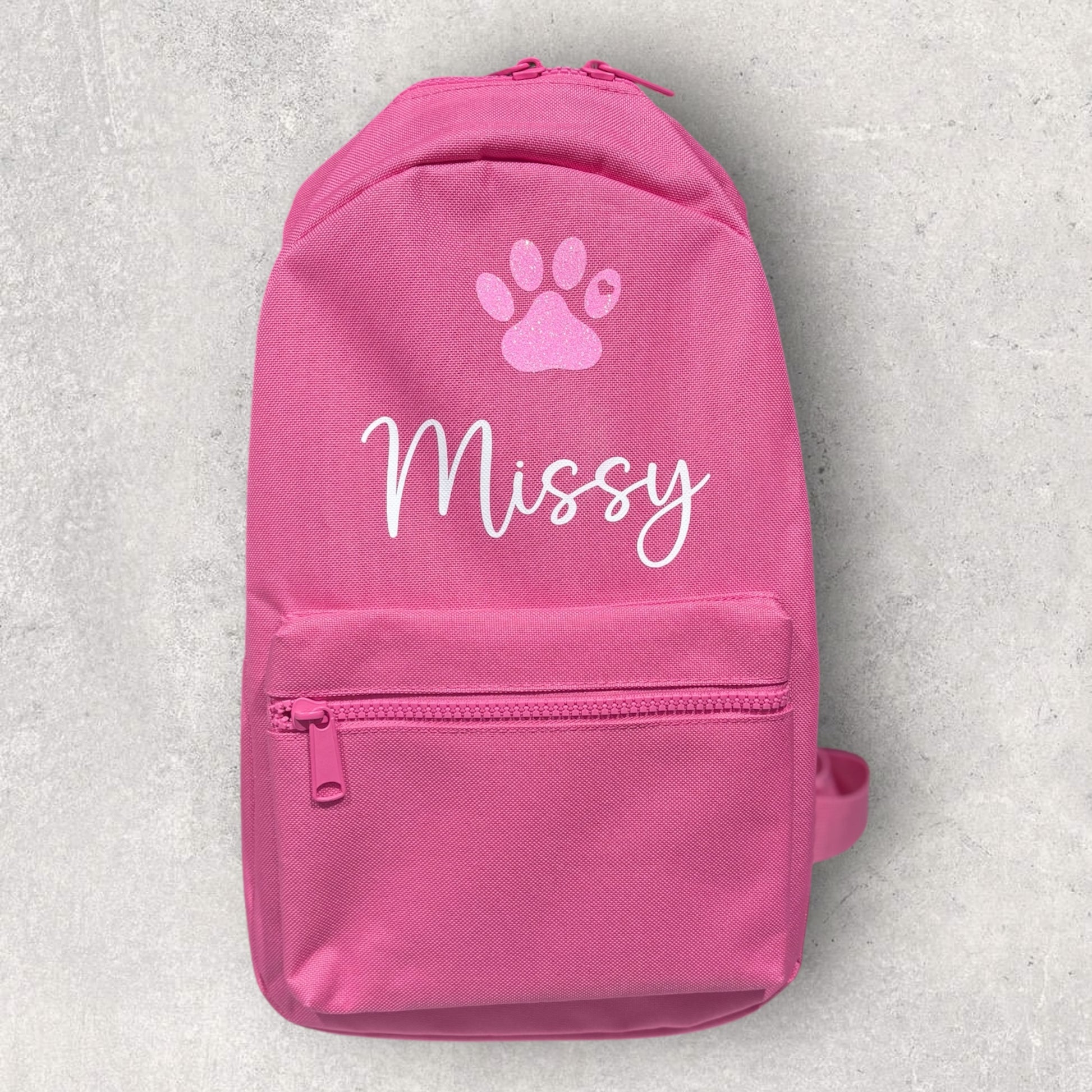 Pink backpack with a paw print and 'Missy' text on a light gray background