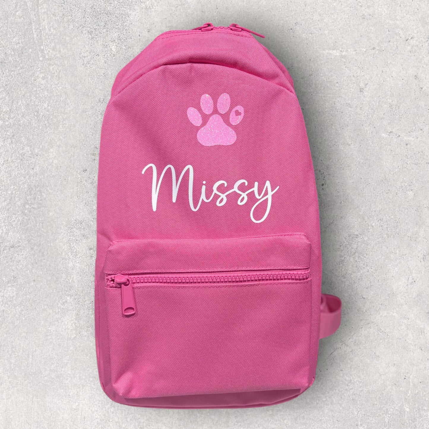 Pink backpack with a paw print and 'Missy' text on a light gray background