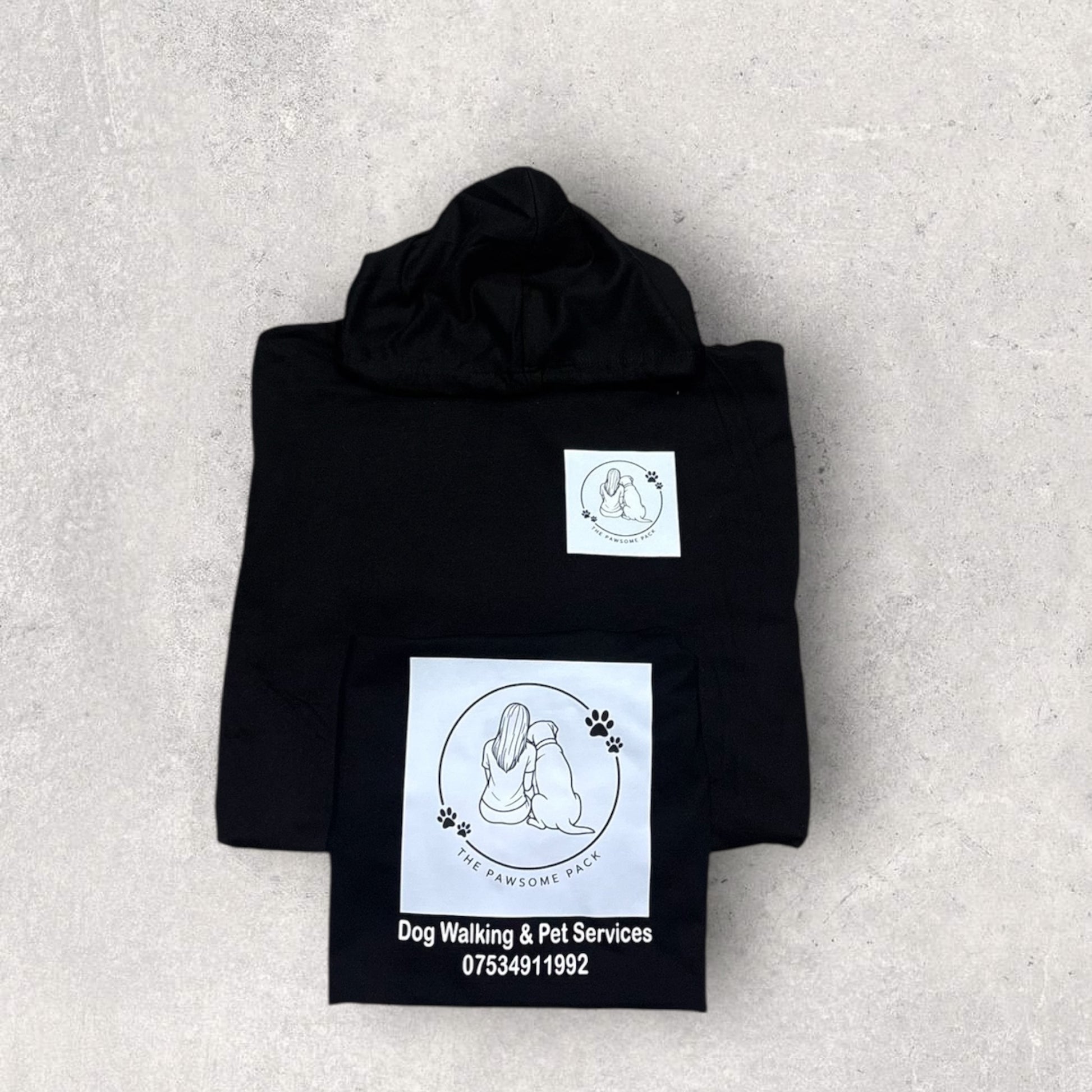 Folded black hoodie with white graphics and text on a light gray background