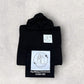 Folded black hoodie with white graphics and text on a light gray background