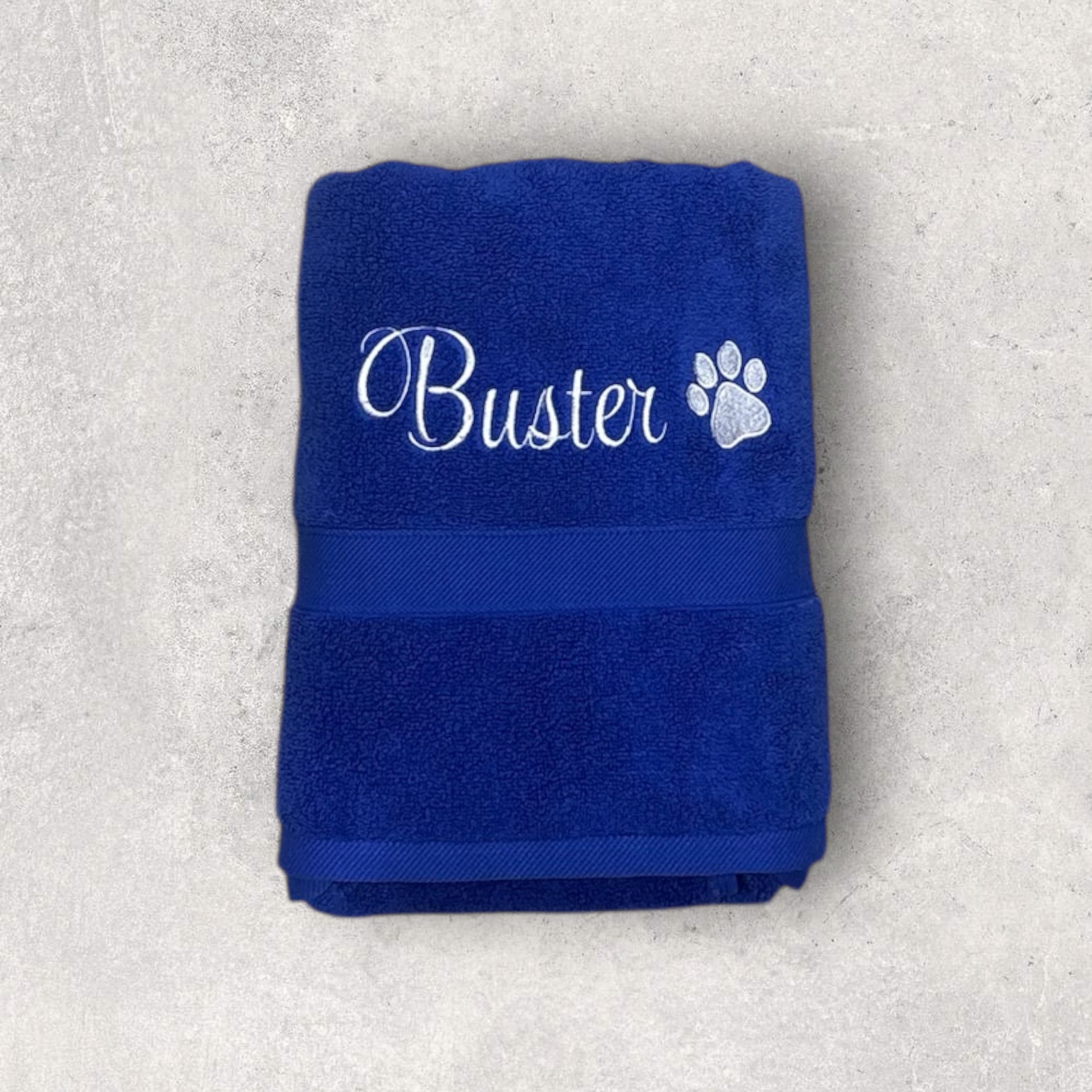 Folded blue towel with 'Buster' and a paw print on a light gray background